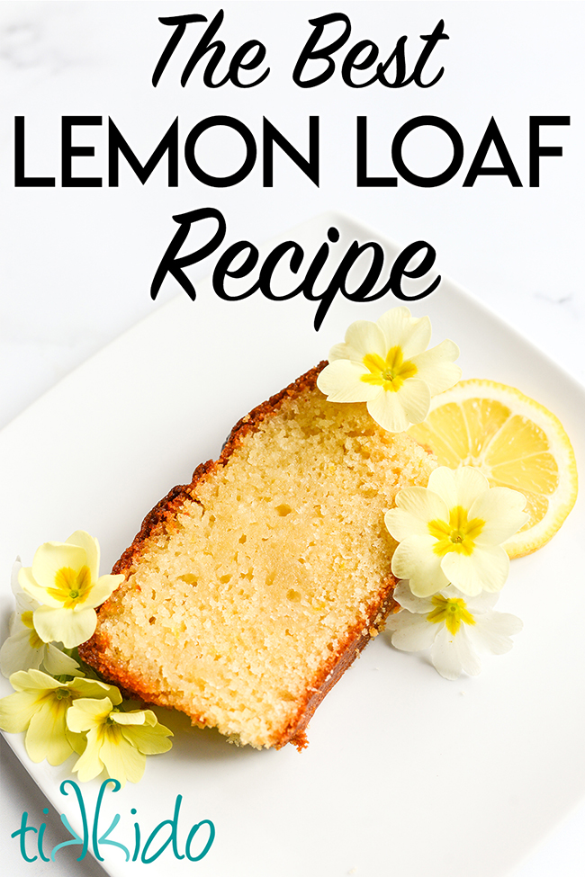 Slice of lemon loaf cake on a white plate with a slice of lemon and edible yellow and white flowers, with text overlay reading "the Best Lemon Loaf Recipe."