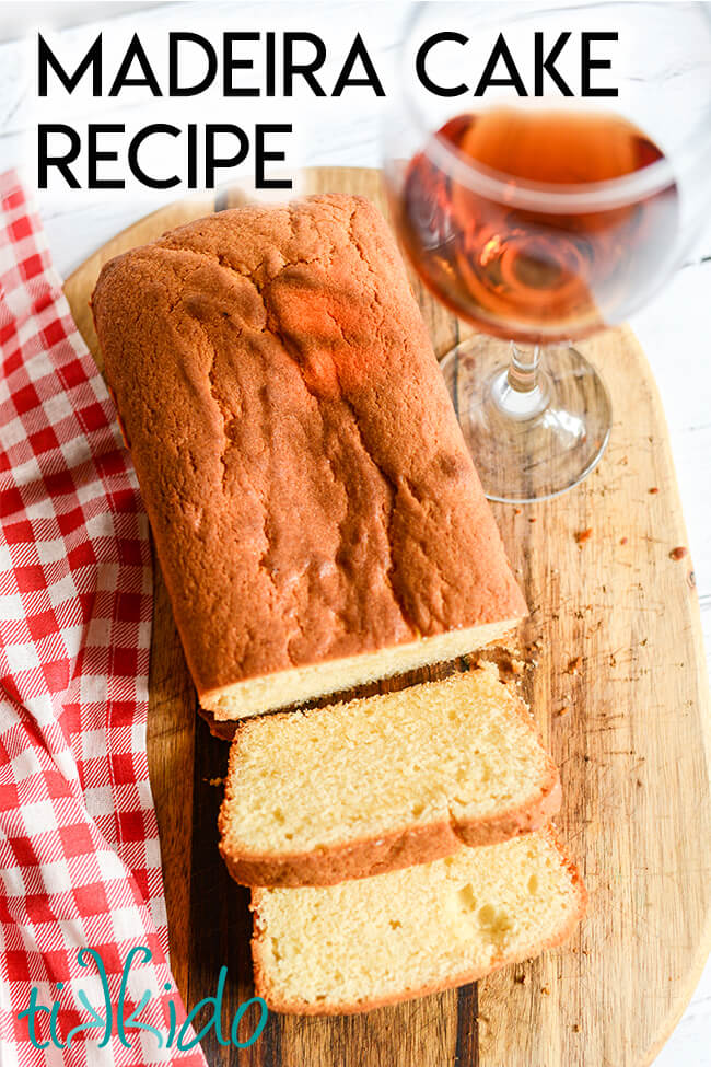 Loaf of Madeira cake with two slices cut off on a wooden cutting board, next to a glass of Madeira wine and a red and white checkered tea towel, with text overlay reading "Madeira Cake Recipe."