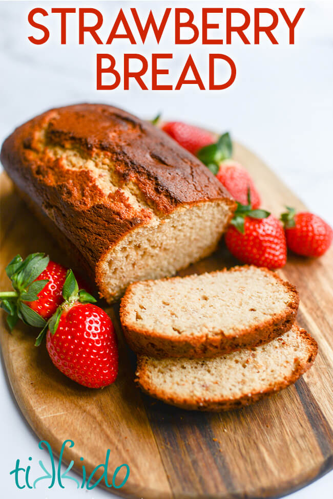 Sliced loaf of strawberry bread on a cutting board, surrounded by fresh strawberries.