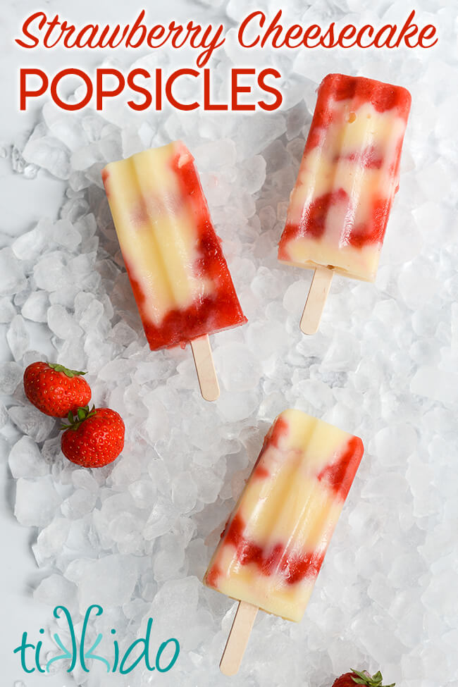 Three Strawberry Cheesecake Popsicles on a bed of ice, next to two fresh strawberries.