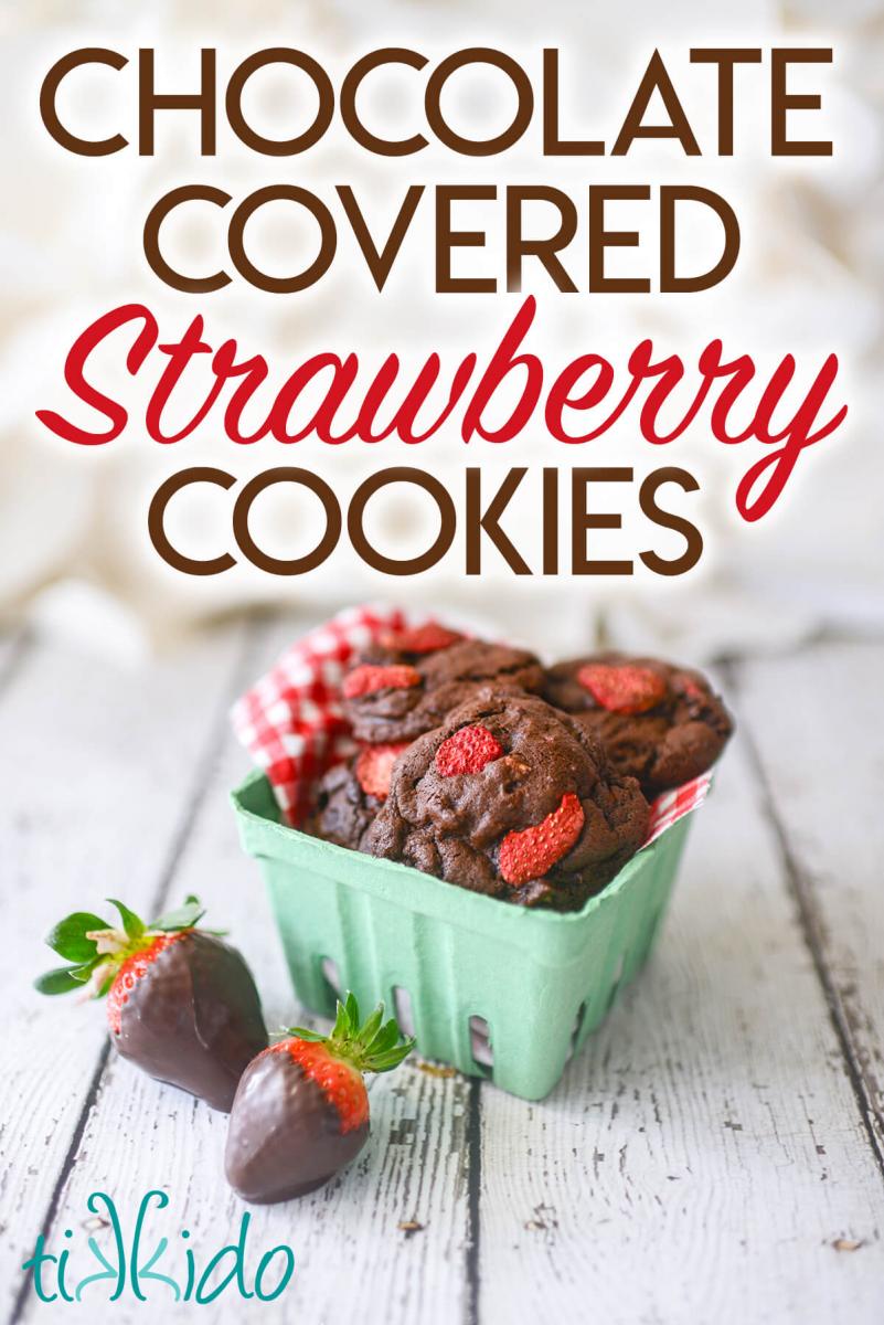 Green strawberry container lined with red and white gingham checked fabric, and filled with chocolate strawberry cookies.  Two classic chocolate covered strawberries sit next to the container.  Text overlay reads "Chocolate covered strawberry cookies."