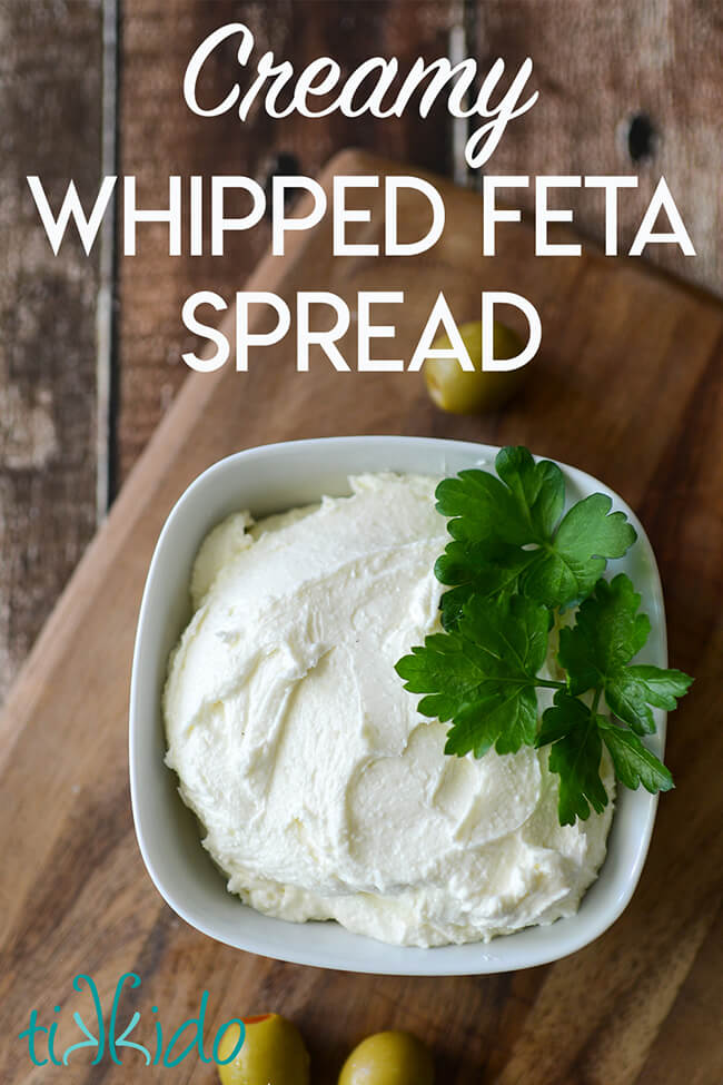 White bowl with creamy whipped feta spread, garnished with fresh parsley, on a wooden cutting board, with text overlay reading "Creamy whipped feta spread."