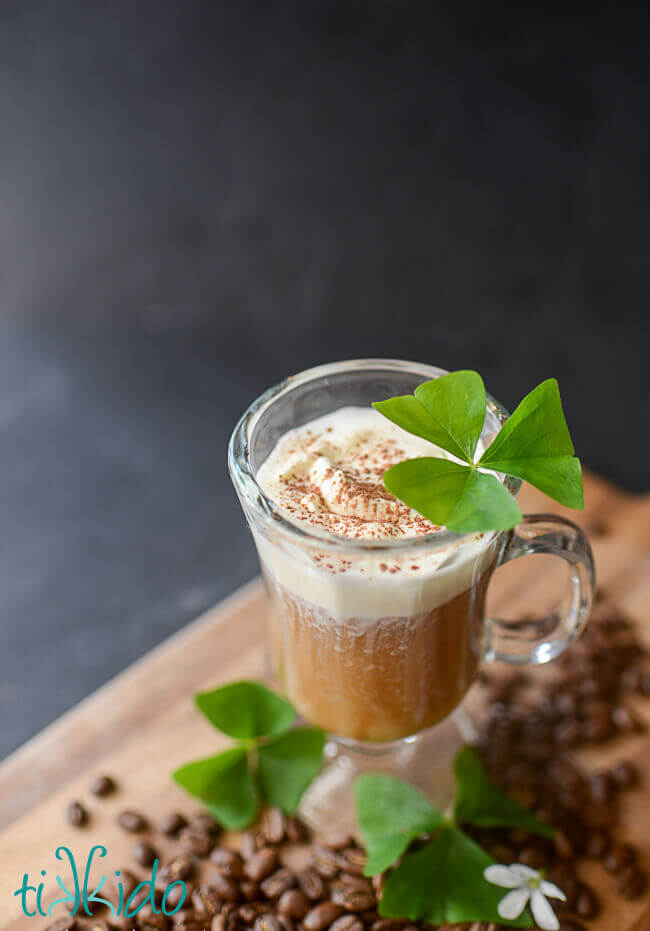 Irish coffee in a clear glass garnished with shamrocks.