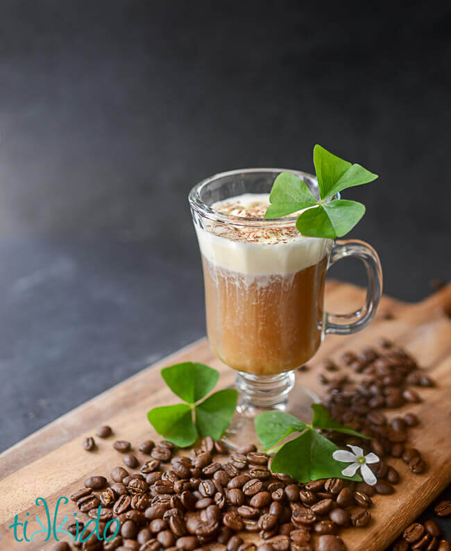 Irish coffee in a clear glass garnished with shamrocks.