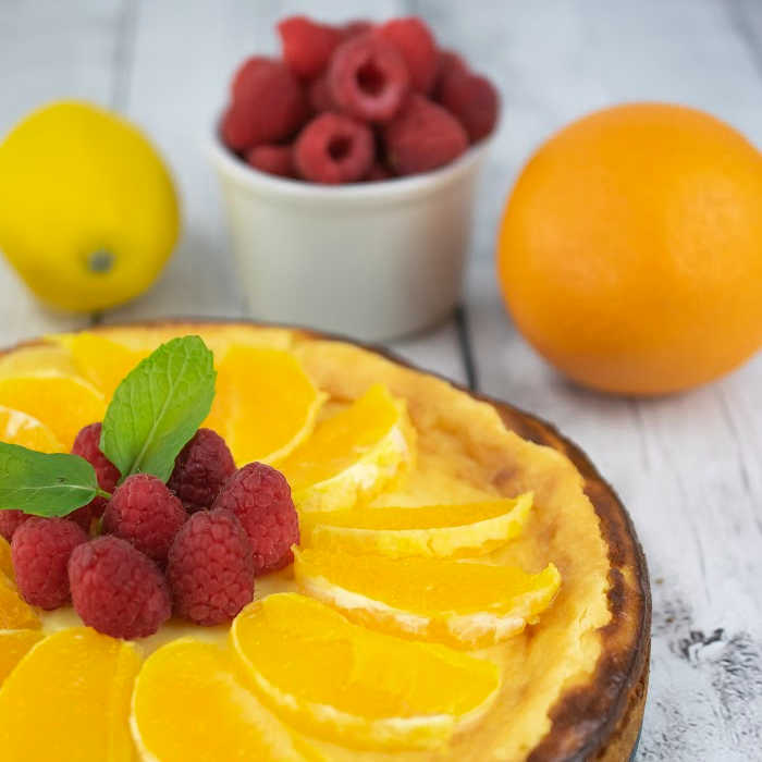Lemon cheesecake topped with slices of fresh orange and raspberries.