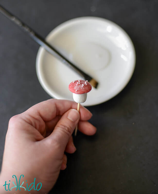 Sprinkles being added to the top of a chocolate mushroom to look like polka dots.