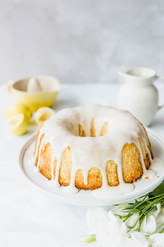 Lemon bundt cake drizzled with lemon glaze on a white cake plate.