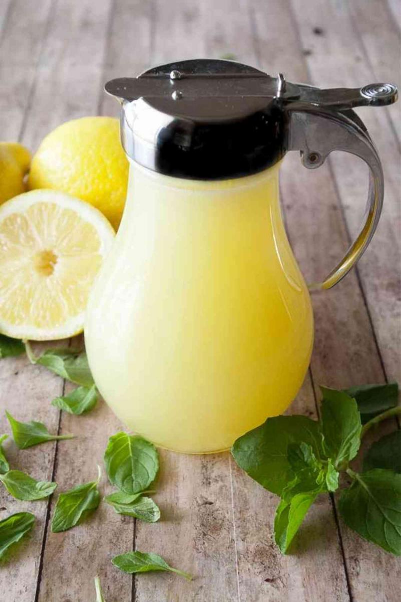 Small pitcher of lemon cream syrup surrounded by fresh mint and sliced lemons.