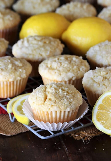 Lemon crumb muffins on a cooling rack, next to whole and sliced lemons.