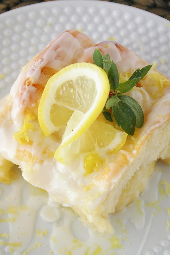 Lemon danish sweet roll on a white plate, topped with a slice of lemon.