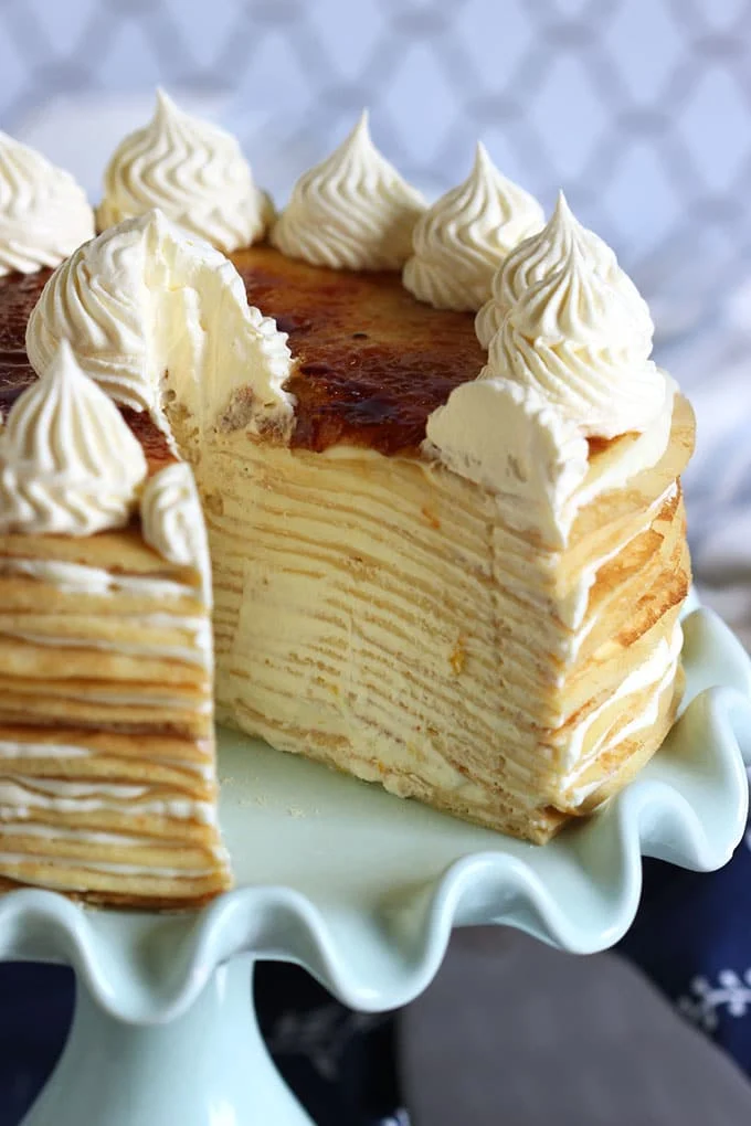 Lemon mascarpone crepe cake on a cake plate with one slice cut out.