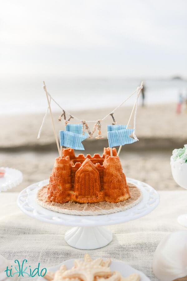 waving flag cake toppers on a sandcastle cake on a table at the beach.