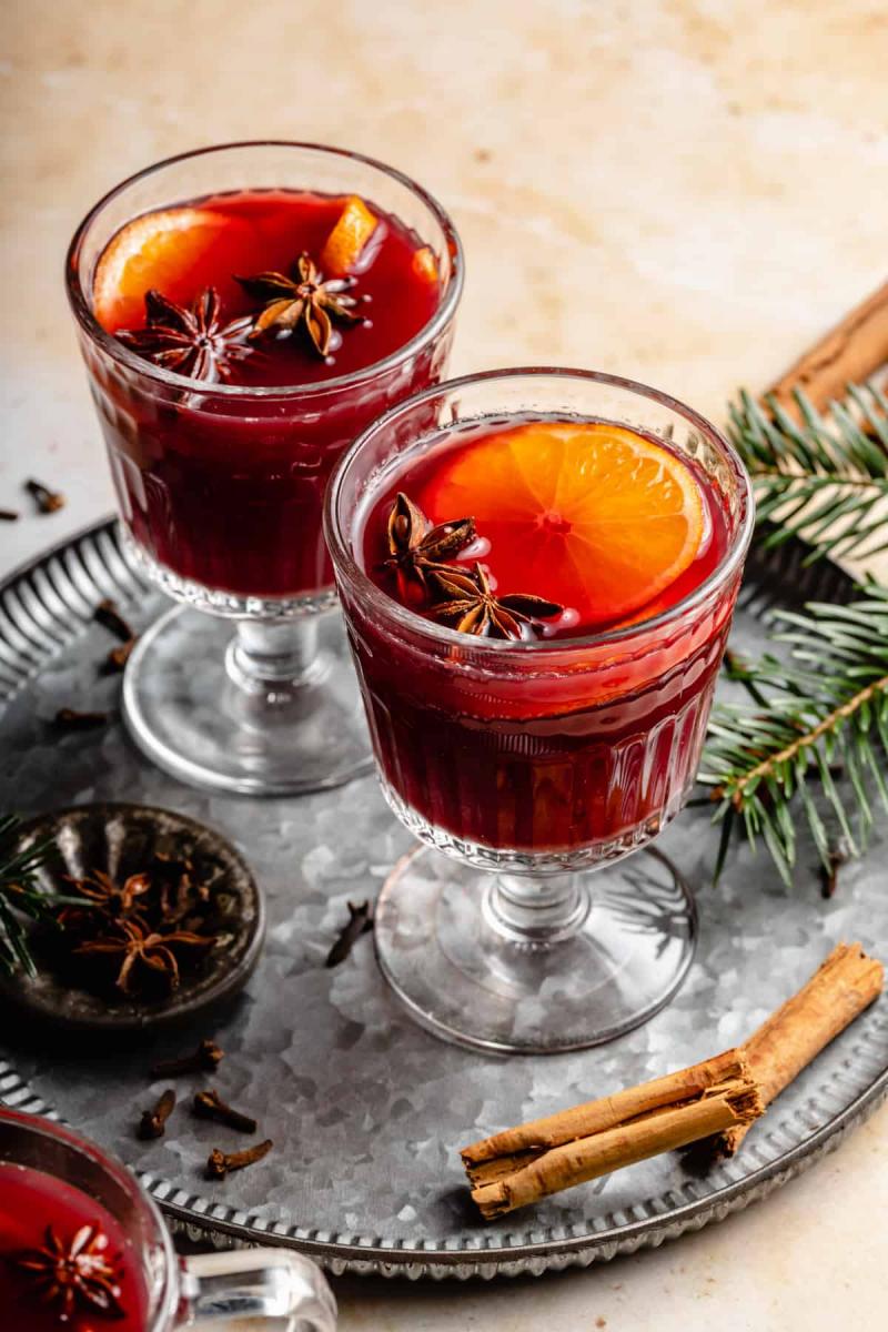 Two glasses of non-alcoholic mulled wine sit on a metal platter.  An orange slice and two star anise pods float in each glass of the punch.