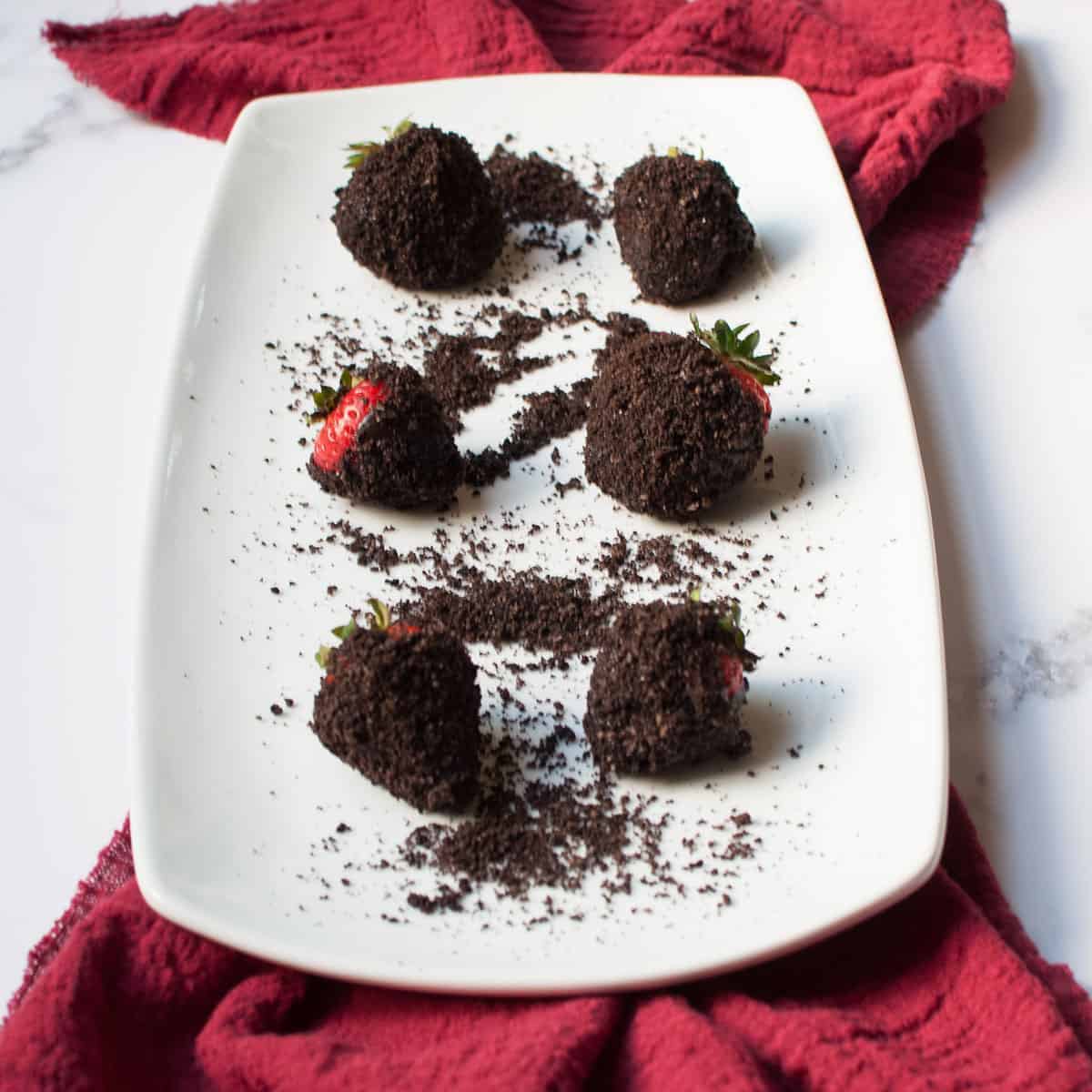 Chocolate covered strawberries rolled in crushed Oreo cookie crumbs on a white plate.