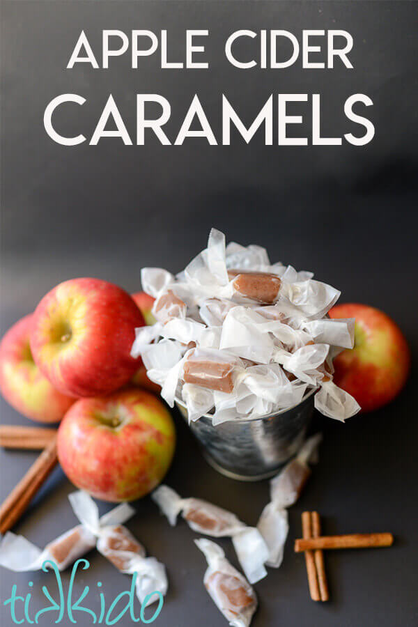 Apple cider caramels in a silver bucket, surrounded by fresh apples and cinnamon sticks.