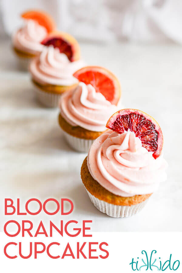 Blood orange cupcakes with naturally pink blood orange frosting, topped with slices of blood orange on a white background.