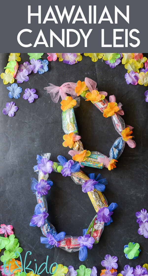 Two candy leis on a black chalkboard background surrounded by colorful silk flowers.