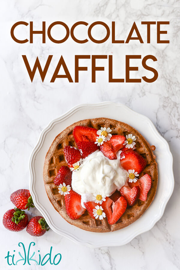 Chocolate waffles topped with strawberries and whipped cream on a white plate.