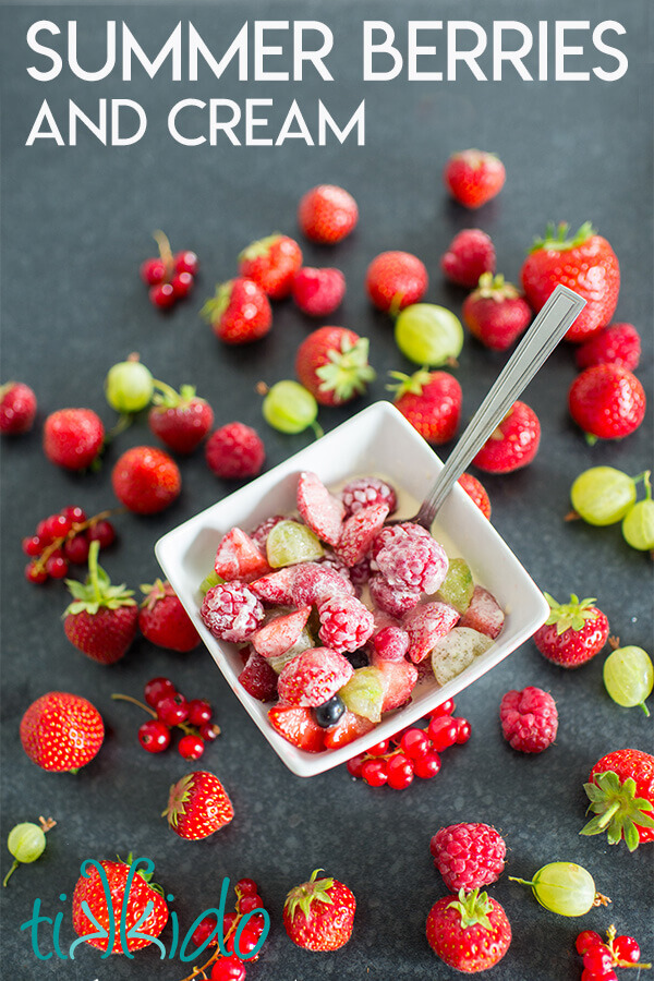 Bowl full of fresh berries and cream, on a black background, surrounded by fresh whole English summer berries.