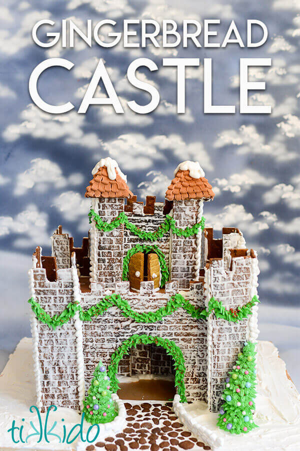 Gingerbread castle decorated with royal icing garlands in front of a snowy painted background.