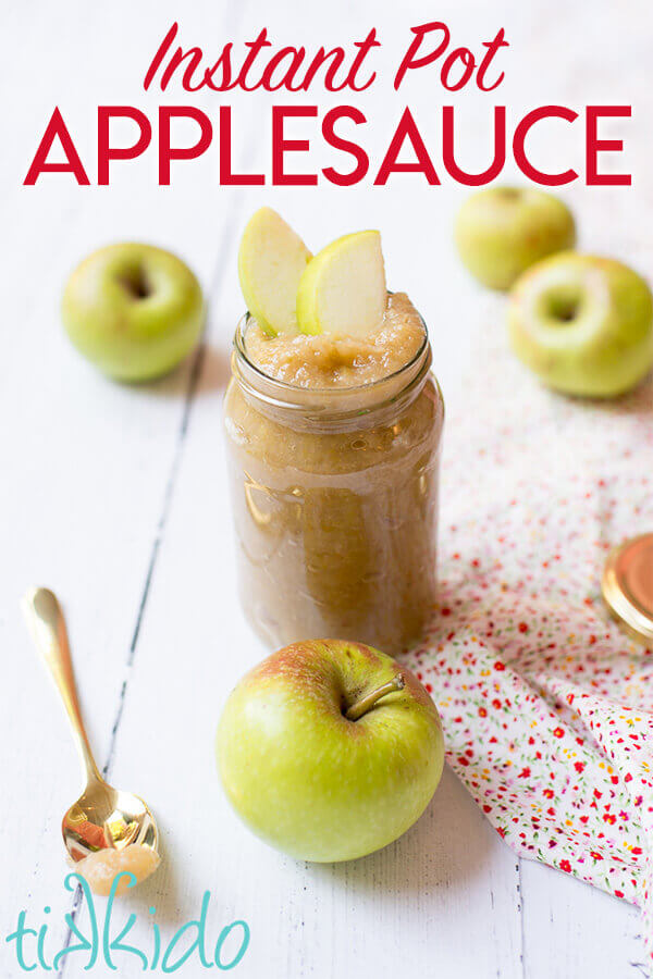 Instant pot applesauce in a clear jar, surrounded by fresh apples on a white wooden table.