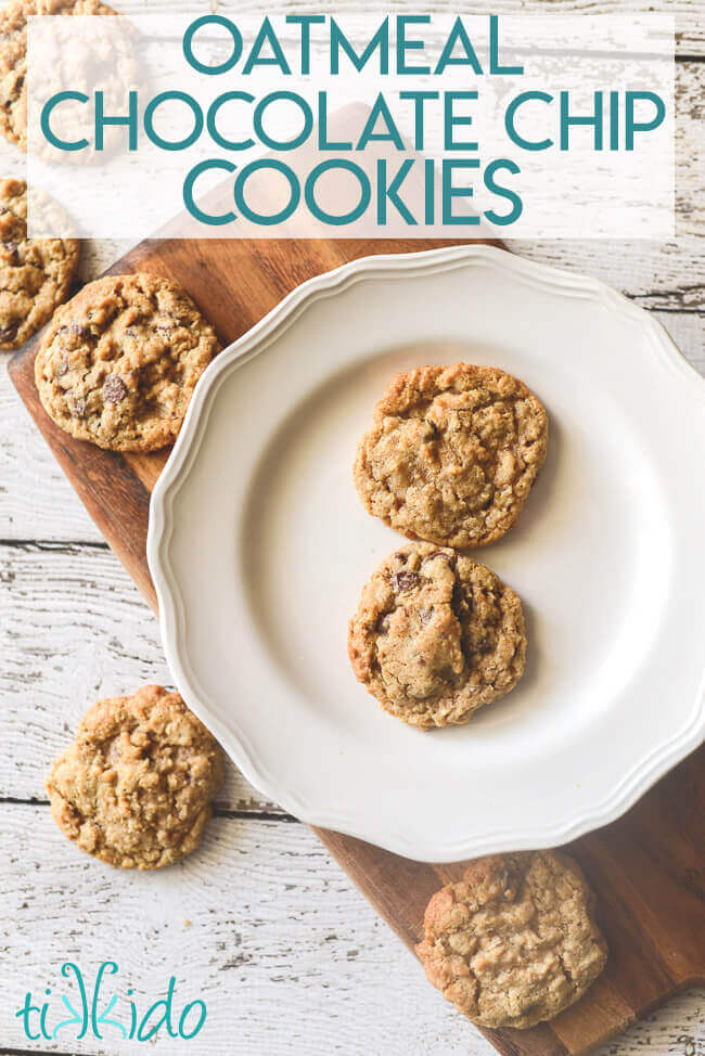 Oatmeal chocolate chip cookies on a white plate, sitting on a cutting board on a white wooden surface.  Extra cookies are scattered around the plate.  Text overlay reads "oatmeal chocolate chip cookies."