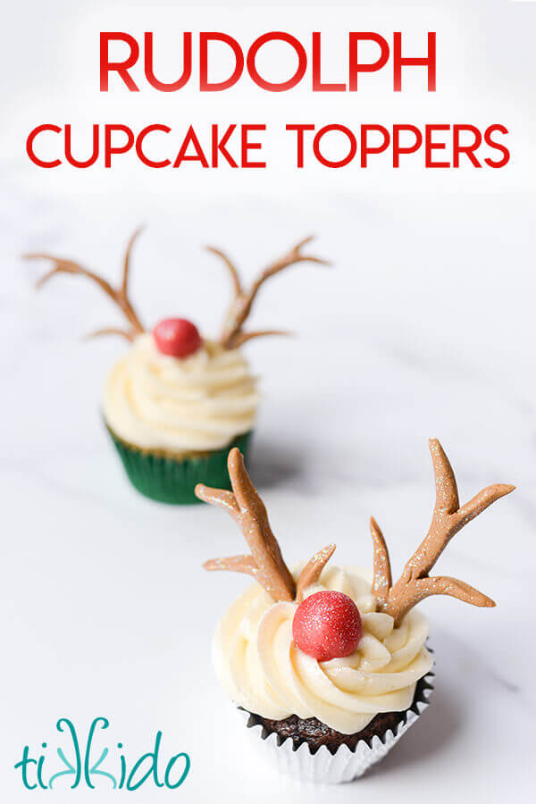 Two reindeer cupcakes with gum paste antlers and red Rudolph noses on a white marble surface.
