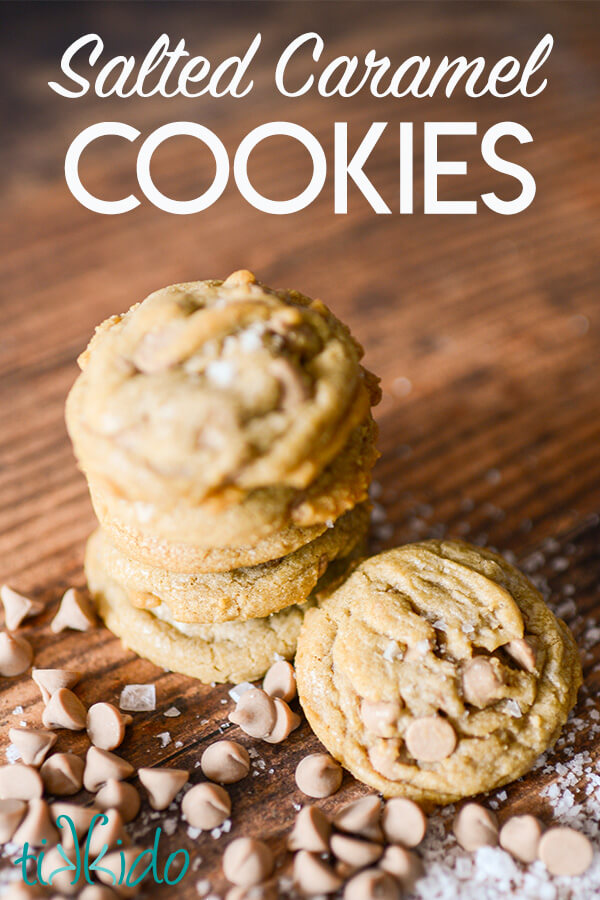 stack of salted caramel cookies on a wooden surface, surrounded by salted caramel baking chips and flakes of sea salt.  Text overlay reads "Salted Caramel Cookies."