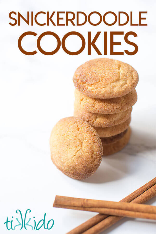 Stack of snickerdoodle cookies next to two sticks of cinnamon on a white marble surface.