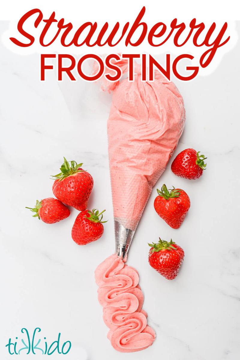 Piping bag filled with strawberry icing, with piped swirls of the icing coming out of the nozzle and fresh strawberries surrounding the bag.  Text overlay reads "Strawberry Frosting."