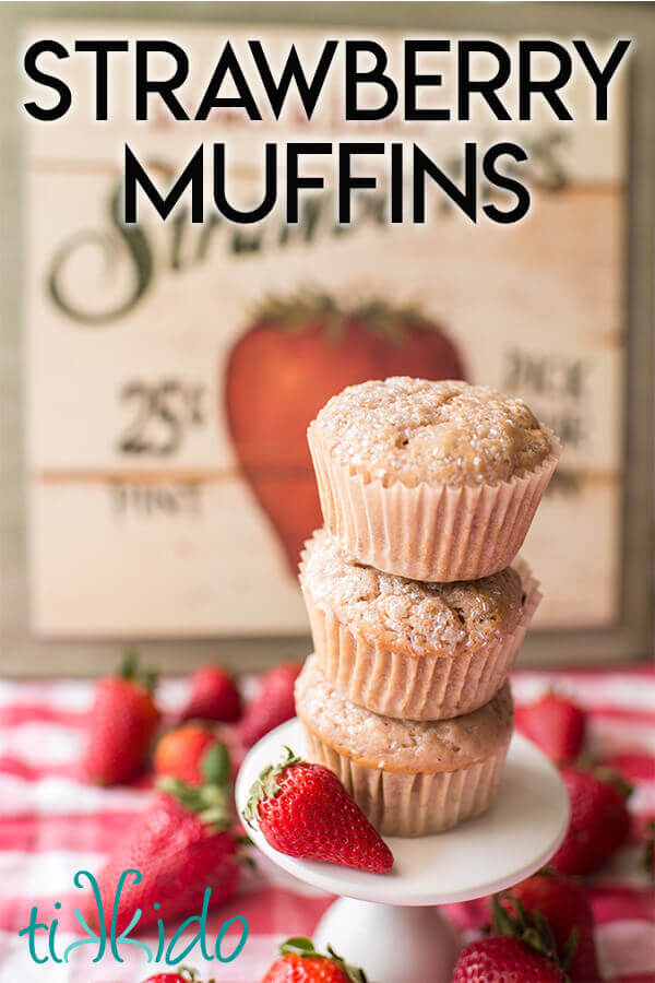 Stack of strawberry muffins surrounded by fresh strawberries on a red gingham tablecloth.