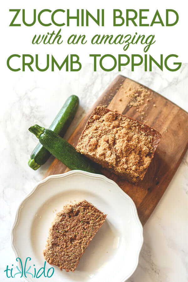 Zucchini bread on a wooden cutting board, with one piece of zucchini bread on a white plate.  Two fresh zucchinis sit next to the board.  Text overlay reads "Zucchini Bread with an amazing Crumb Topping."