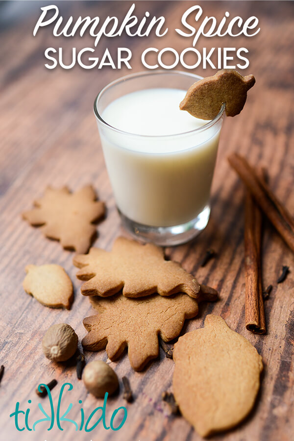 Pumpkin spice cut out sugar cookies on a wooden table surrounded by whole spices and a glass of milk, with the text overlay reading "Pumpkin Spice Sugar Cookies."