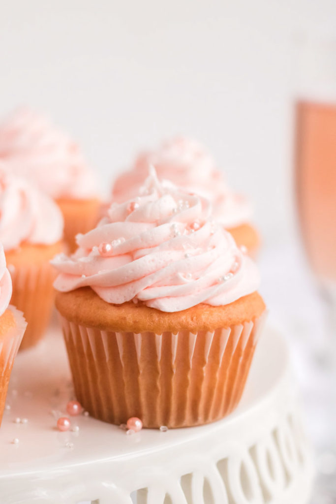 Pink champagne cupcakes on a white cake stand.