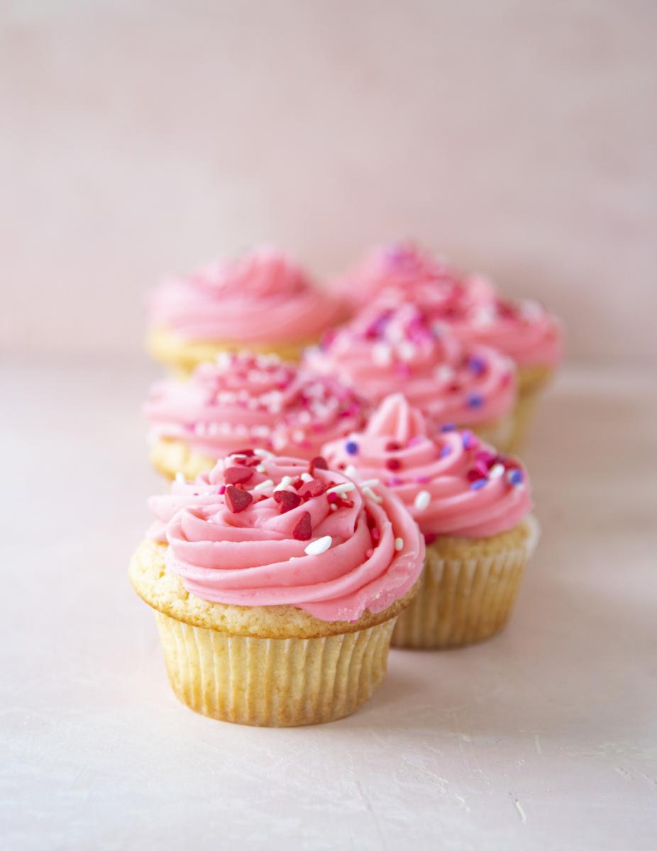 Vanilla cupcakes topped with pink frosting and sprinkles.