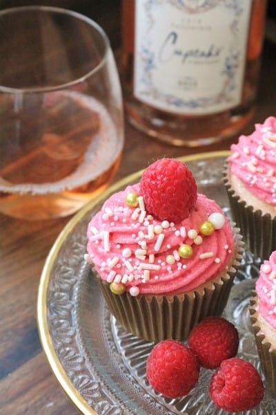 Raspberry Rosé Cupcakes topped with fresh raspberries and sprinkles, next to a glass of Rosé wine.