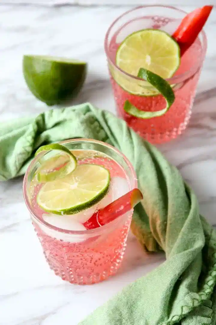 Two glasses of rhubarb gin and tonic, a beautiful pink cocktail garnished with fresh lime and rhubarb.