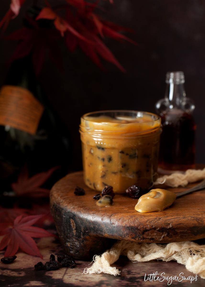 Rum raisin caramel sauce Ice Cream Topping in a glass jar, on a wooden serving tray.