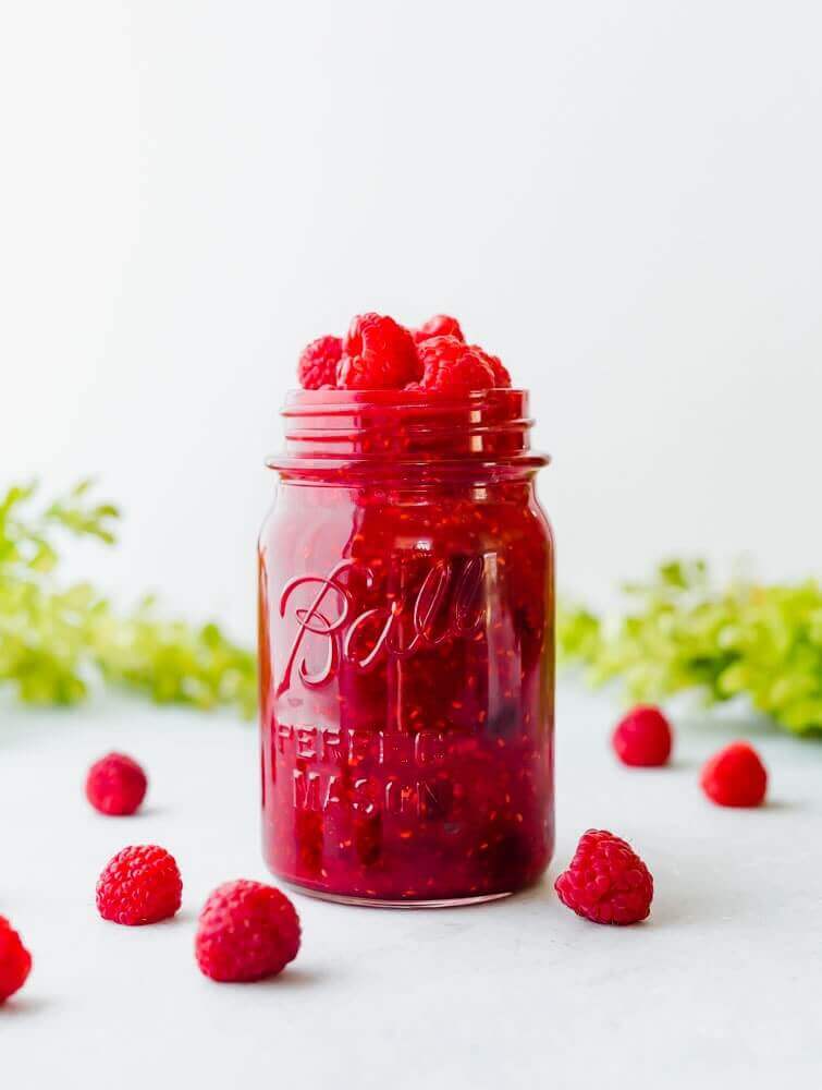 Raspberry sauce Ice Cream Topping in a glass Ball jar, surrounded by fresh raspberries.