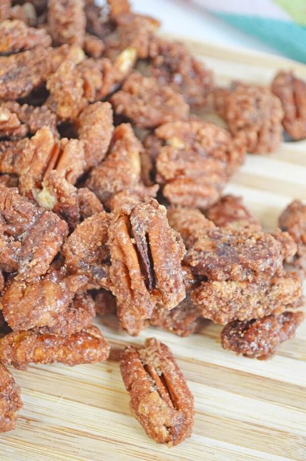 Crock Pot Candied pecans in a pile on a wooden cutting board.