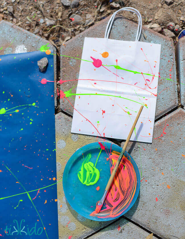 Plain wrapping paper and gift bags being splatter painted with neon paint to make Splatter Paint Wrapping Paper