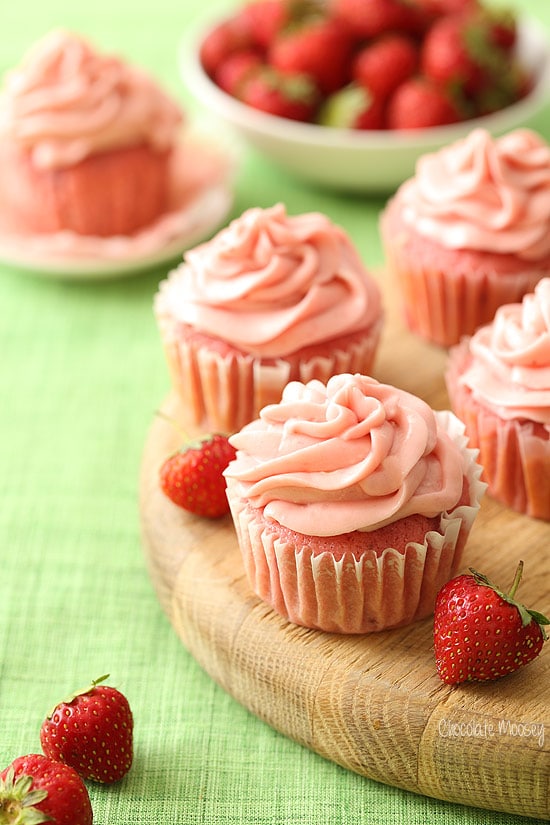 Small batch strawberry cupcakes on a wooden cutting board next to fresh strawberries.