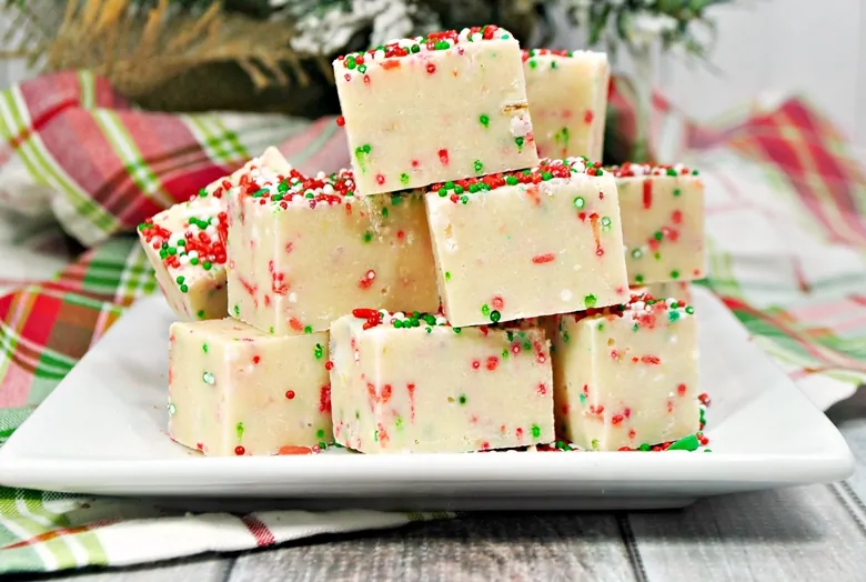 Sugar cookie Christmas fudge stacked on a white plate.