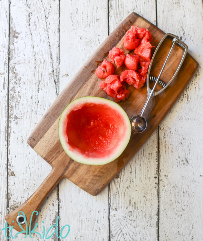Watermelon scooped out of its shell with a melon baller scoop, on a wooden cutting board.