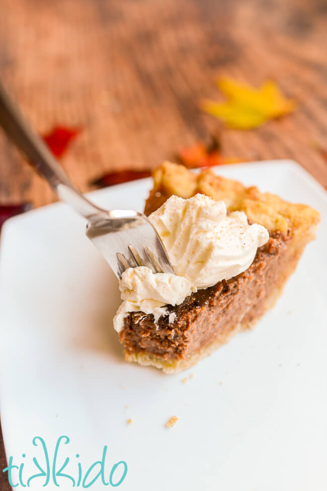 Fork taking a bite out of a piece of apple butter pie topped with whipped cream.