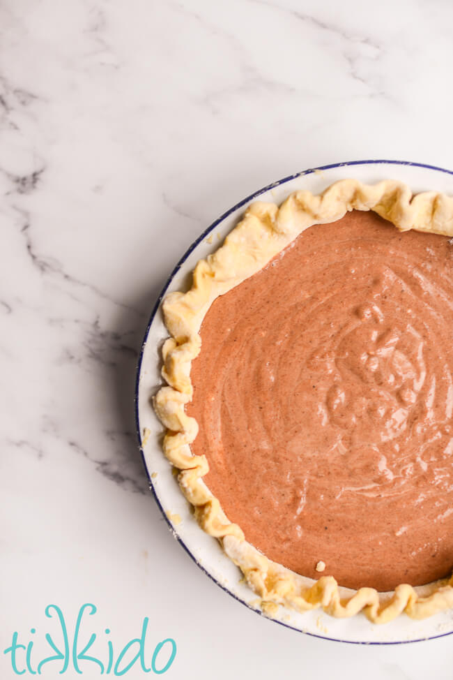 Custard for apple butter pie, unbaked and in a single pie crust, on a white marble surface.