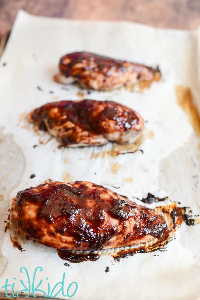 Cherry barbecue sauce on three baked chicken breasts on parchment paper.