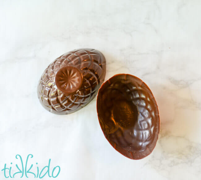 Two separate halves of a large, hollow, chocolate Easter egg on a white marble surface.