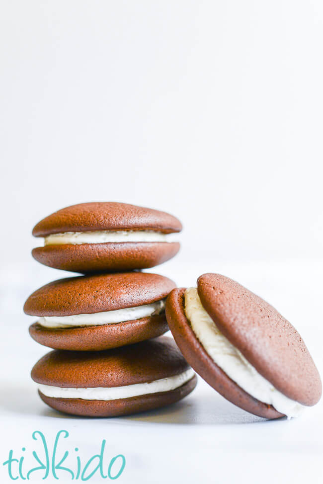 Four chocolate whoopie pies stacked on a white surface.