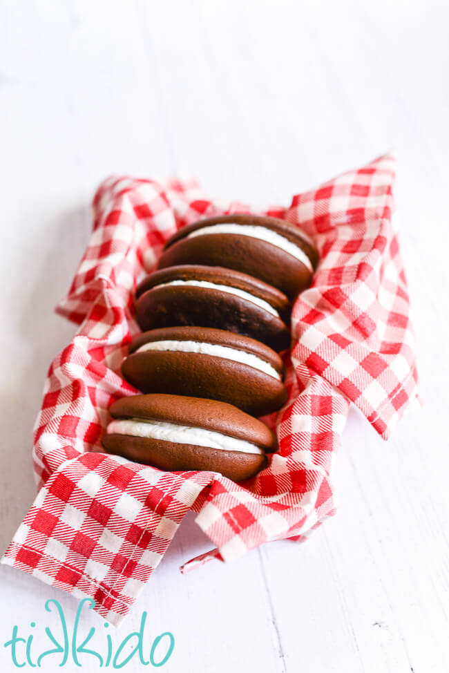 Four chocolate whoopie pies in a container lined with a red and white checked napkin.